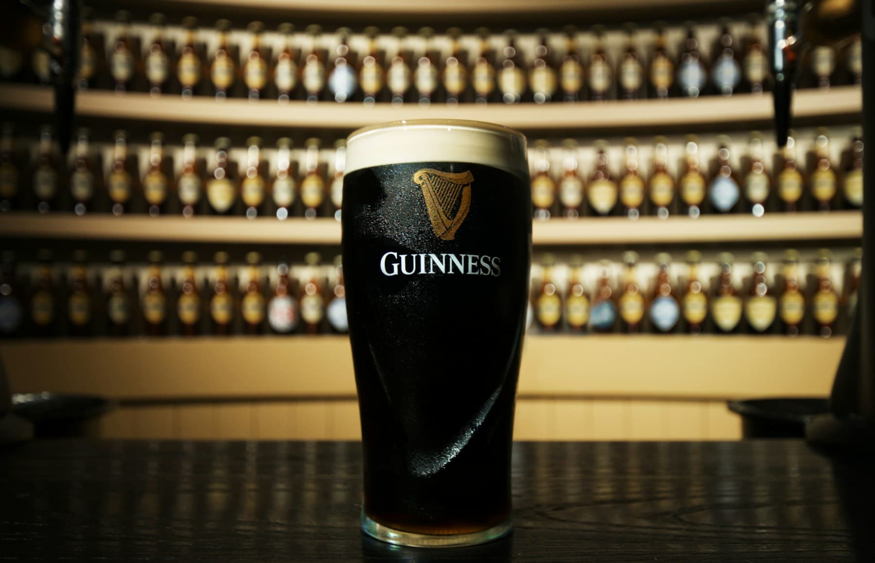 A pint of Guinness on a table in front of shelves of bottles